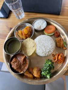 A round brass plate holds a variety of dishes including a mound of white rice, a serving of yogurt, and several small bowls containing different items.