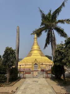 
A golden stupa stands majestically against a clear blue sky, flanked by palm trees. 