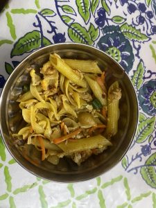 A metal bowl filled with penne and shell pasta mixed with shredded carrots and diced green chilies.