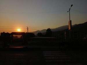 Sunset over Butwal, with warm orange light behind mountain and building silhouettes and power lines across the sky.