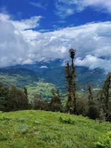 A beautiful view of green hills and valleys under a bright blue sky with white clouds in Jiri, Nepal.
