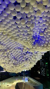 A dense, cloud-like installation of hundreds of white globes suspended from a ceiling and illuminated by blue light.