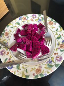 A plate with vibrant pink dragon fruit, cut into small cubes, is placed on a decorative white plate with floral patterns.