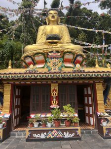 A large golden statue of a seated Buddha is prominently displayed in front of a colorful temple adorned with intricate decorations. 