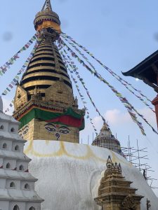 
A view of a large stupa topped with a golden spire and colorful prayer flags fluttering in the breeze. 
