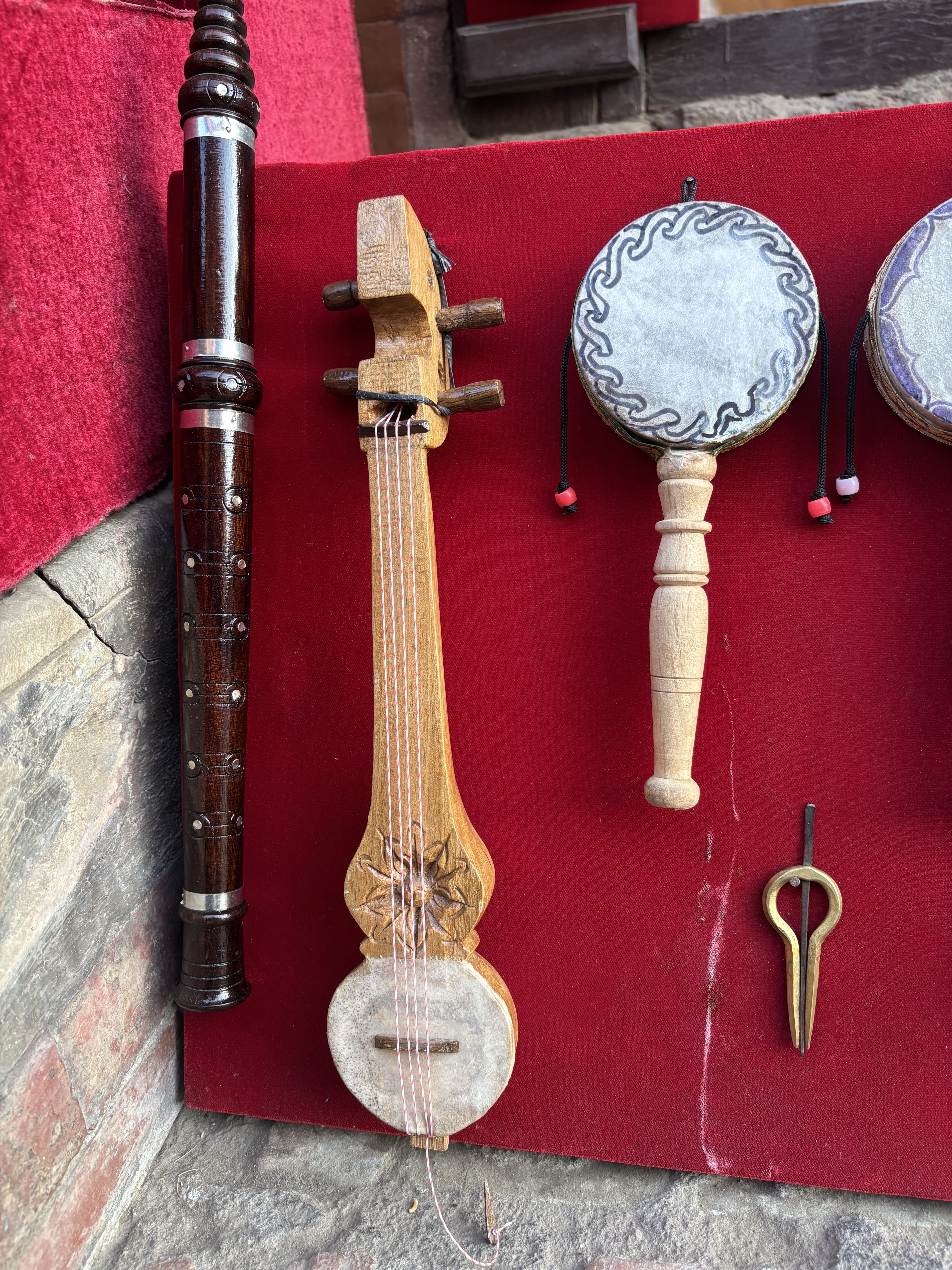 A close-up of traditional musical instruments displayed on red fabric, including a flute, stringed instrument, hand drums, and a jaw harp.