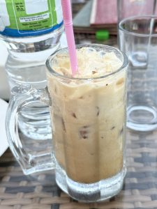 A frosty glass of creamy iced coffee with ice cubes and a pink straw.