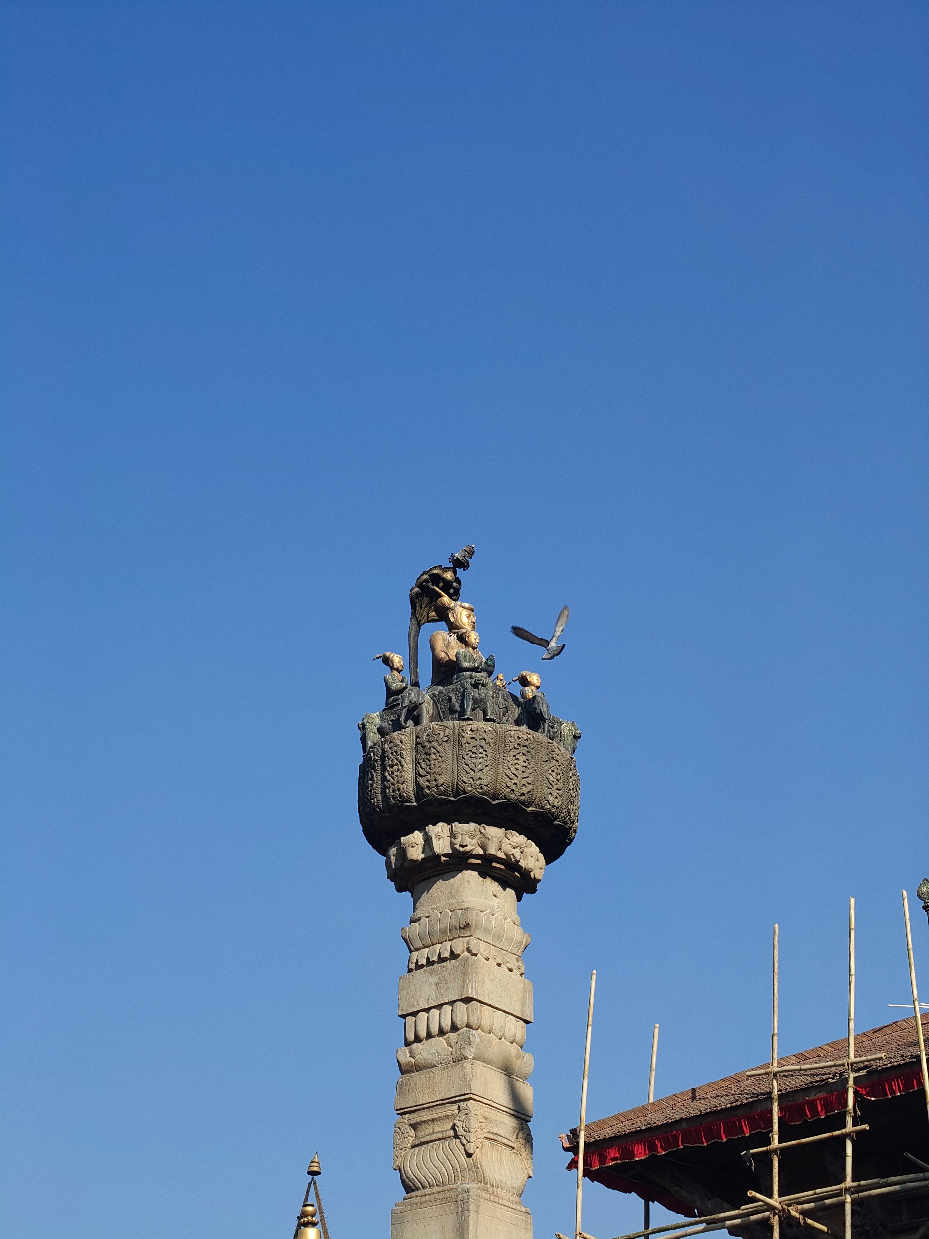 A tall stone pillar topped with an intricately carved statue featuring a figure with a bird and several smaller figures.