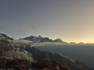 A panoramic view of snow-capped mountains under a twilight sky, with soft clouds hovering just above the valley.