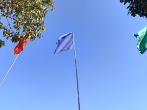 A clear blue sky serves as the backdrop for three flags flying on poles.