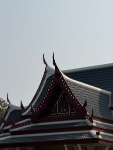 A traditional Southeast Asian temple with an ornate roof, pointed spires, and red and dark blue tiles, set against a clear sky.
