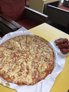 A large pizza with a golden crust, topped with melted cheese and pieces of cooked chicken, is displayed on a round platter.