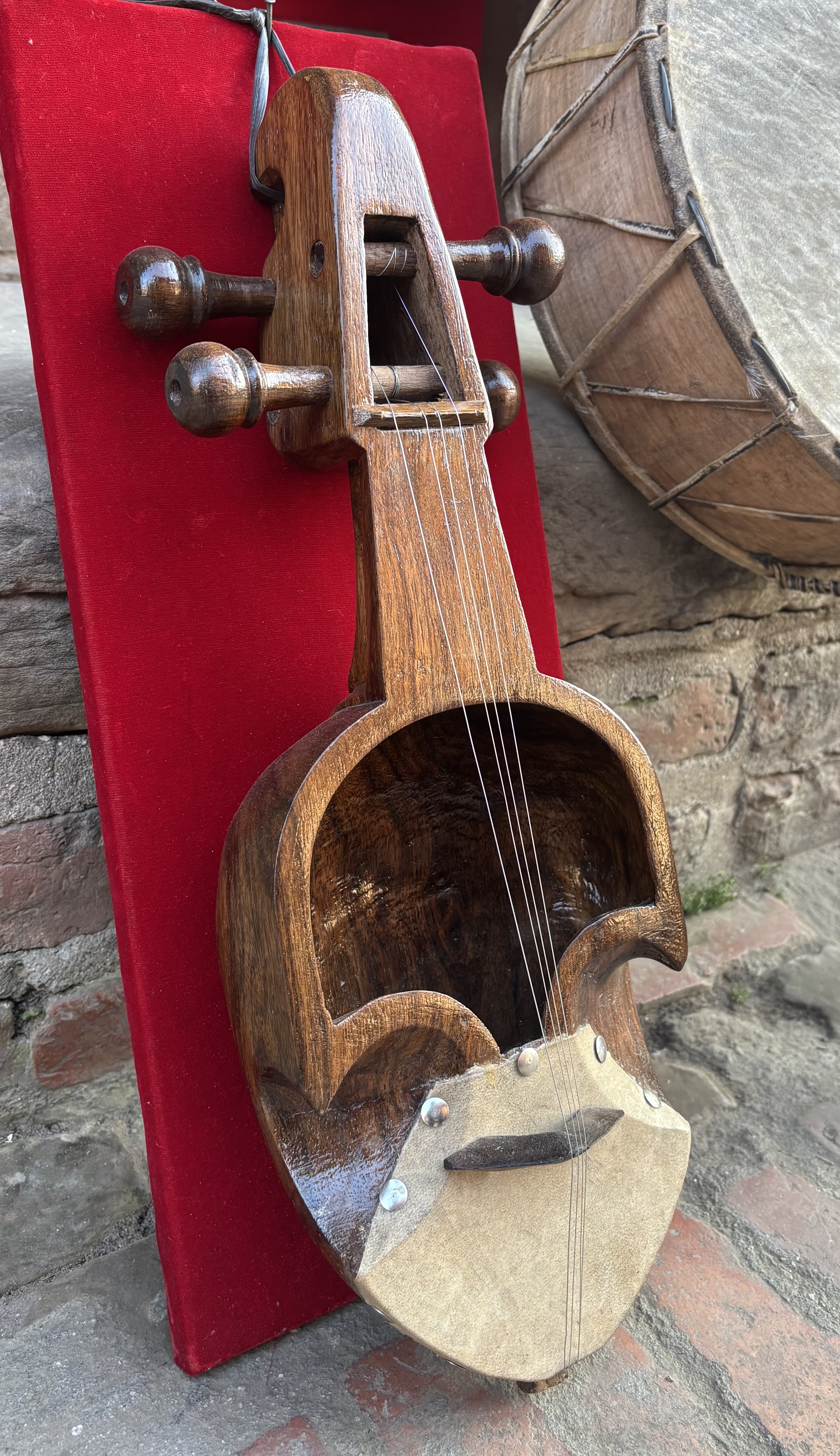 A traditional Sarangi with a curved wooden body and strings is displayed on a red background.