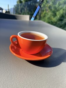 A vibrant orange cup filled with tea sits on a matching saucer, placed on a gray surface.