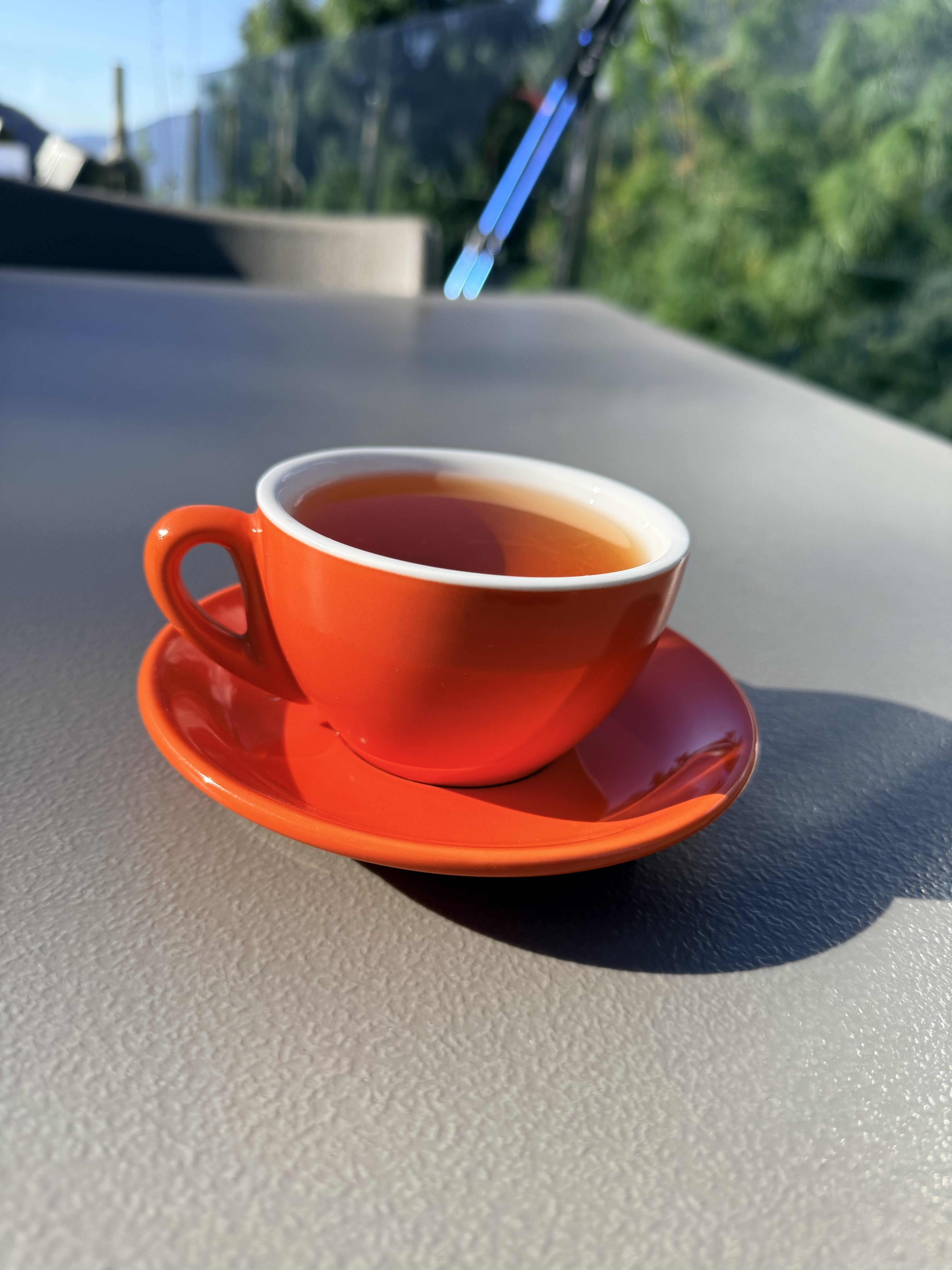 A vibrant orange cup filled with tea sits on a matching saucer, placed on a gray surface.