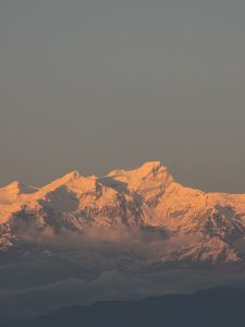 A breathtaking view of snow-capped mountains at sunrise, with sunlight illuminating the peaks and casting a warm glow on the landscape. 