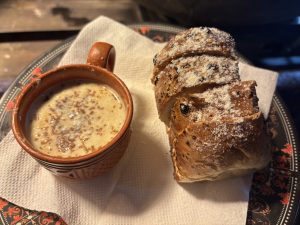 A warm, creamy spiced tea with a freshly baked, sugar-dusted pastry on a rustic plate.

