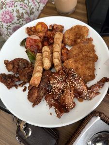 A white plate filled with a variety of appetizers, including fried chicken pieces, a breaded fish fillet, and various sauces. 
