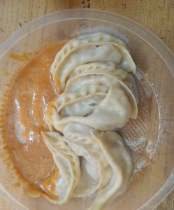 An asian cusine, dumplings (Momo) placed on a plastic plate with tomato sauce on its side on the wooden table.