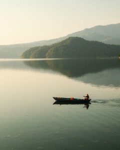 A solitary boat glides across a calm lake, with a person paddling in the center. The atmosphere is tranquil and peaceful, capturing the essence of nature.