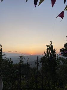 A serene sunset view over distant mountains, with the sun partially dipping below the horizon