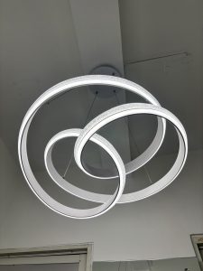 A modern chandelier composed of three intertwined circular rings, illuminated with white light.