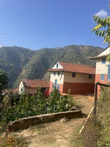 A scenic rural landscape featuring two houses with colorful exteriors&mdash;one predominantly white with blue windows and another that is peach-colored