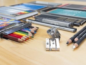 A photograph of drawing pencils that include graphite, ranging from H to B pencils, colored pencils, woodless pencils, matt pencils, and a pencil sharpener.