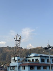 A clear sky frames a view of a mountain peak covered in snow, located behind a blue building with multiple windows and rooftop greenery.