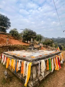 A stone Buddhist stupa decorated with orange marigold petals on top and surrounded by colorful prayer scarves in yellow, white, and red.