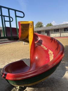 A colorful playground slide in red and yellow, with a green railing. 