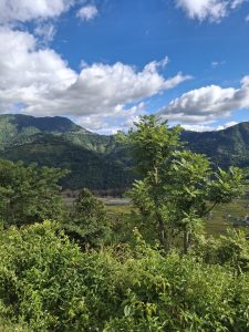 
A scenic landscape featuring rolling green hills and mountains under a partly cloudy blue sky.
