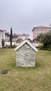 A small stone house with a slanted roof sits on a grassy lawn.