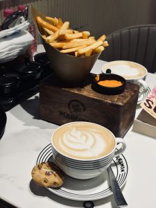 
A cup of coffee with a decorative latte art sits on a black-and-white striped saucer next to a cookie.