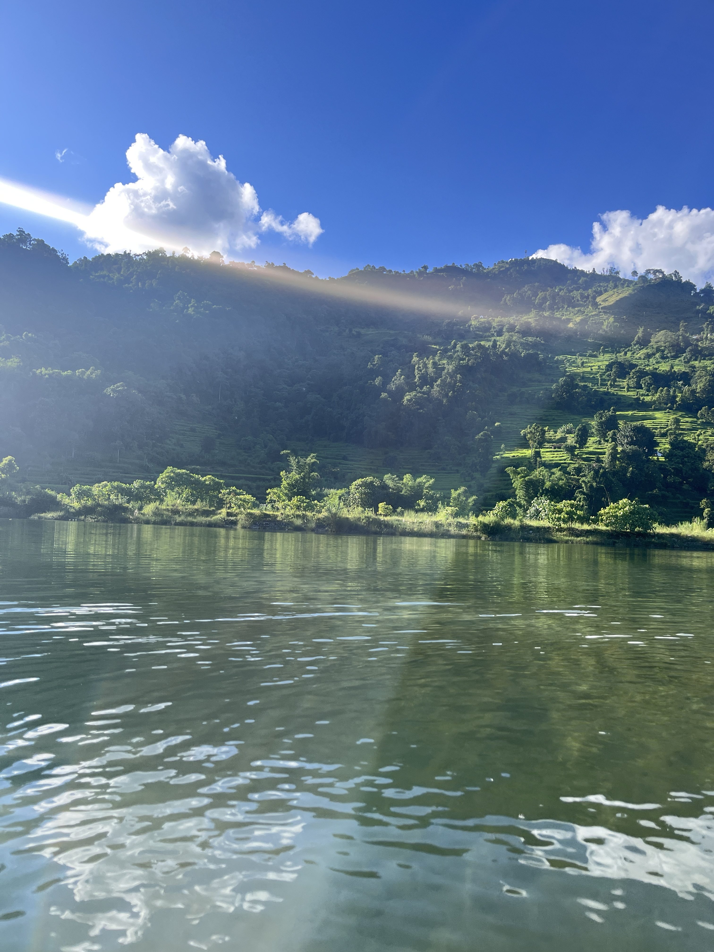 A serene landscape featuring a calm body of water reflecting the sky, surrounded by lush greenery on sloping hills