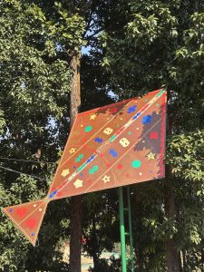 A colorful kite is displayed on a vertical pole surrounded by lush green trees. 