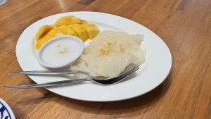 A delicious serving of Thai mango sticky rice on a white plate, with fresh mango slices and a small bowl of coconut cream.
