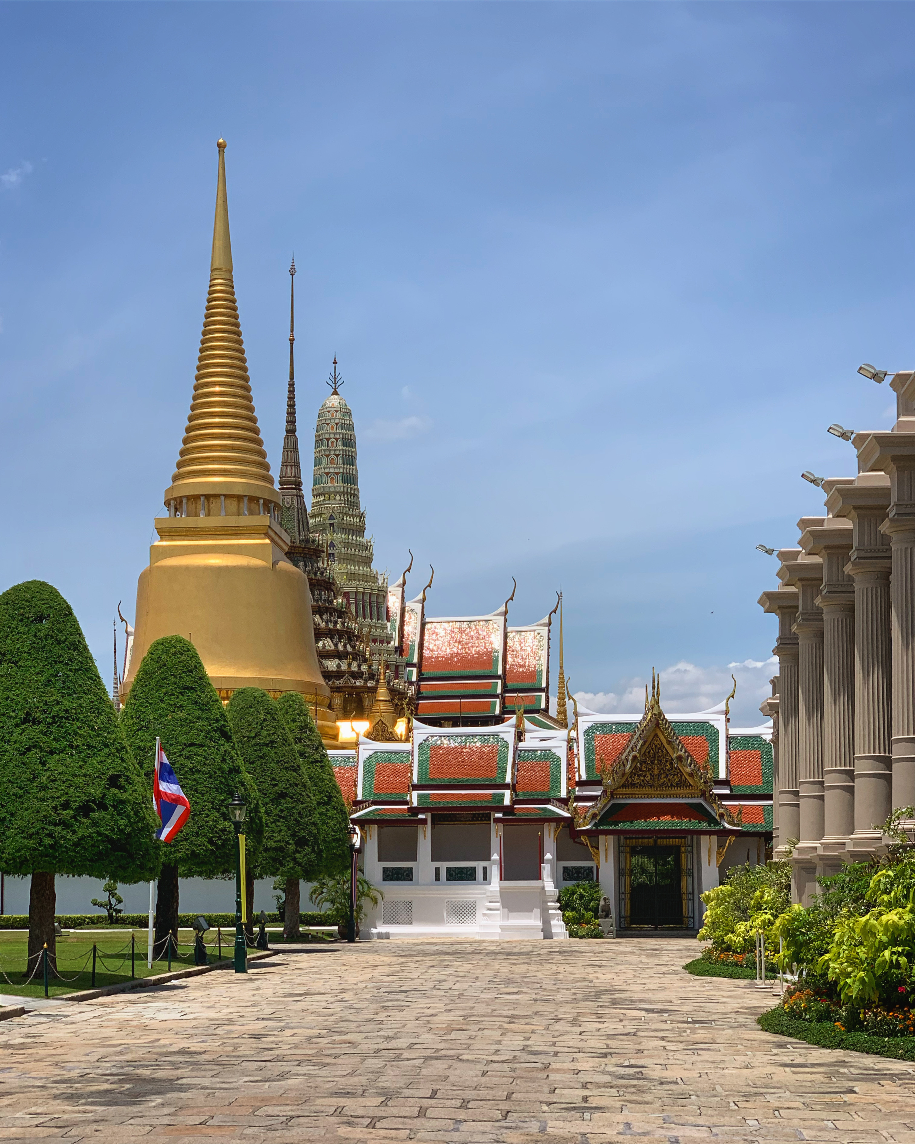 The image showcases the Grand Palace and Wat Phra Kaeo in Bangkok, Thailand. Prominent features include the golden spire of Phra Si Rattana Chedi and the ornate, multi-tiered roofs of the Temple of the Emerald Buddha. Traditional Thai architecture includes intricate details and vibrant red, green, and gold colors.