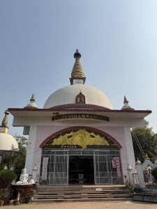 
A prominent white stupa with a golden spire stands tall against a clear blue sky. 
