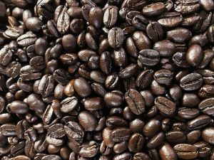 A close-up view of a pile of dark roasted coffee beans, showcasing their glossy, rich appearance and varying shapes, set against a dark backdrop.