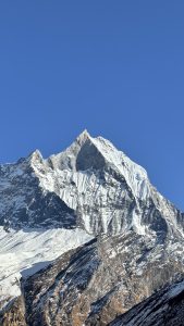 A tall, snow-capped mountain peak rises against a clear blue sky. 