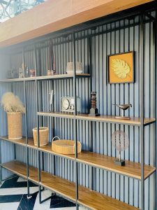 A modern shelf with wooden boards holds decorative items: baskets, dry grass, a vintage radio, sculptures, and framed art. The tone is stylish and cozy.