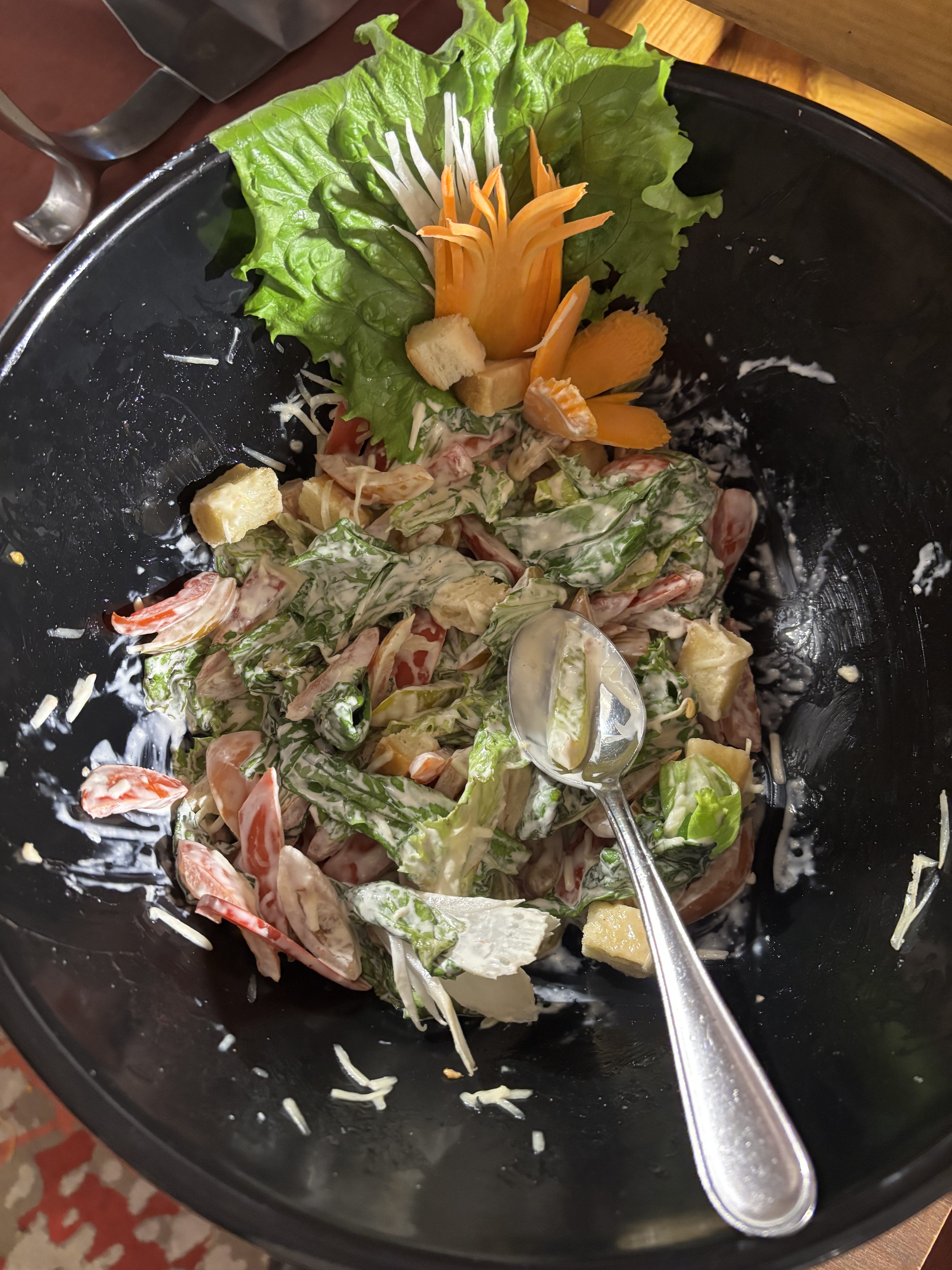 A large black bowl filled with a colorful salad consisting of fresh lettuce, sliced tomatoes, croutons, and a creamy dressing. 