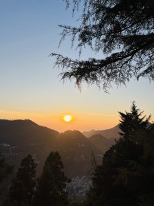A sunset view over mountainous terrain, with the sun casting a warm orange glow. 