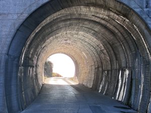 A concrete tunnel with a circular arch, leading to bright light at the far end.