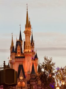 Fairytale castle illuminated at dusk, glowing with warm lights against a soft evening sky.