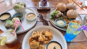 
A colorful dining setup featuring various dishes on wooden tables. In the foreground, a plate of crispy fried food accompanied by a small dish of dipping sauce.