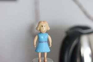A small plastic figurine of a girl stands atop a cylindrical object.
