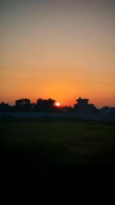 A sunset scene featuring a vibrant orange sun sinking below the horizon, surrounded by a gradient of soft pastel colors in the sky.