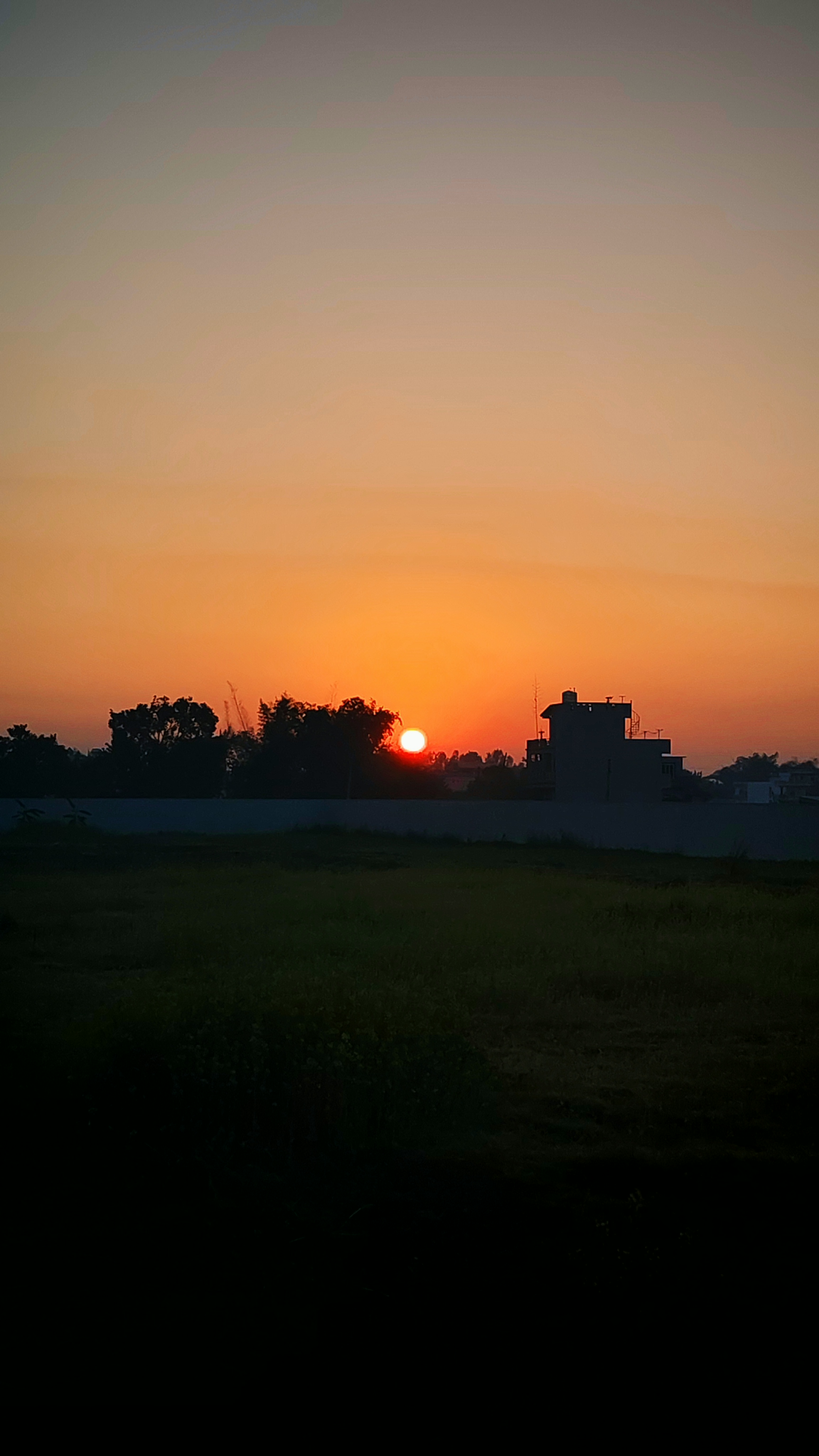 A sunset scene featuring a vibrant orange sun sinking below the horizon, surrounded by a gradient of soft pastel colors in the sky.